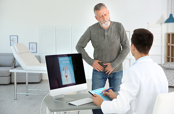A man is standing in front of his doctor's desk and pointing to his groin area while the doctor takes notes 